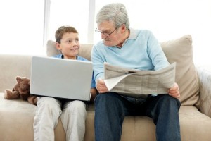 Elderly man sitting with a newspaper while a smiling little boy